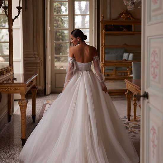 
Expertly crafted, Tiffani is an A-line wedding dress with a sleek high-thigh slit, detachable sleeves, and an illusion sweetheart neckline. Made from luxurious silk tulle and adorned with delicate beading, it exudes timeless elegance for your special day.